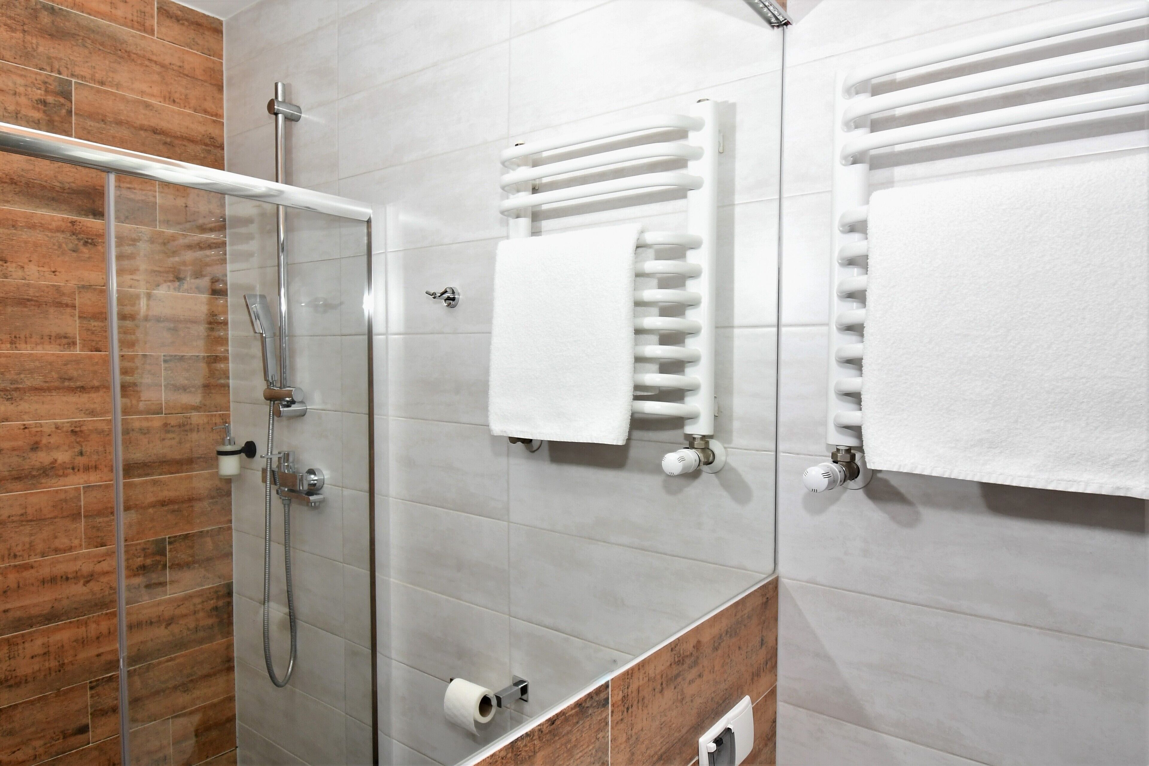 Un baño moderno con cabina de ducha de vidrio, toalleros blancos y una pared decorativa de madera.