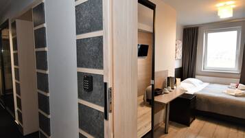 Una habitación de hotel con cama, mesita de noche y armario con televisión integrada.