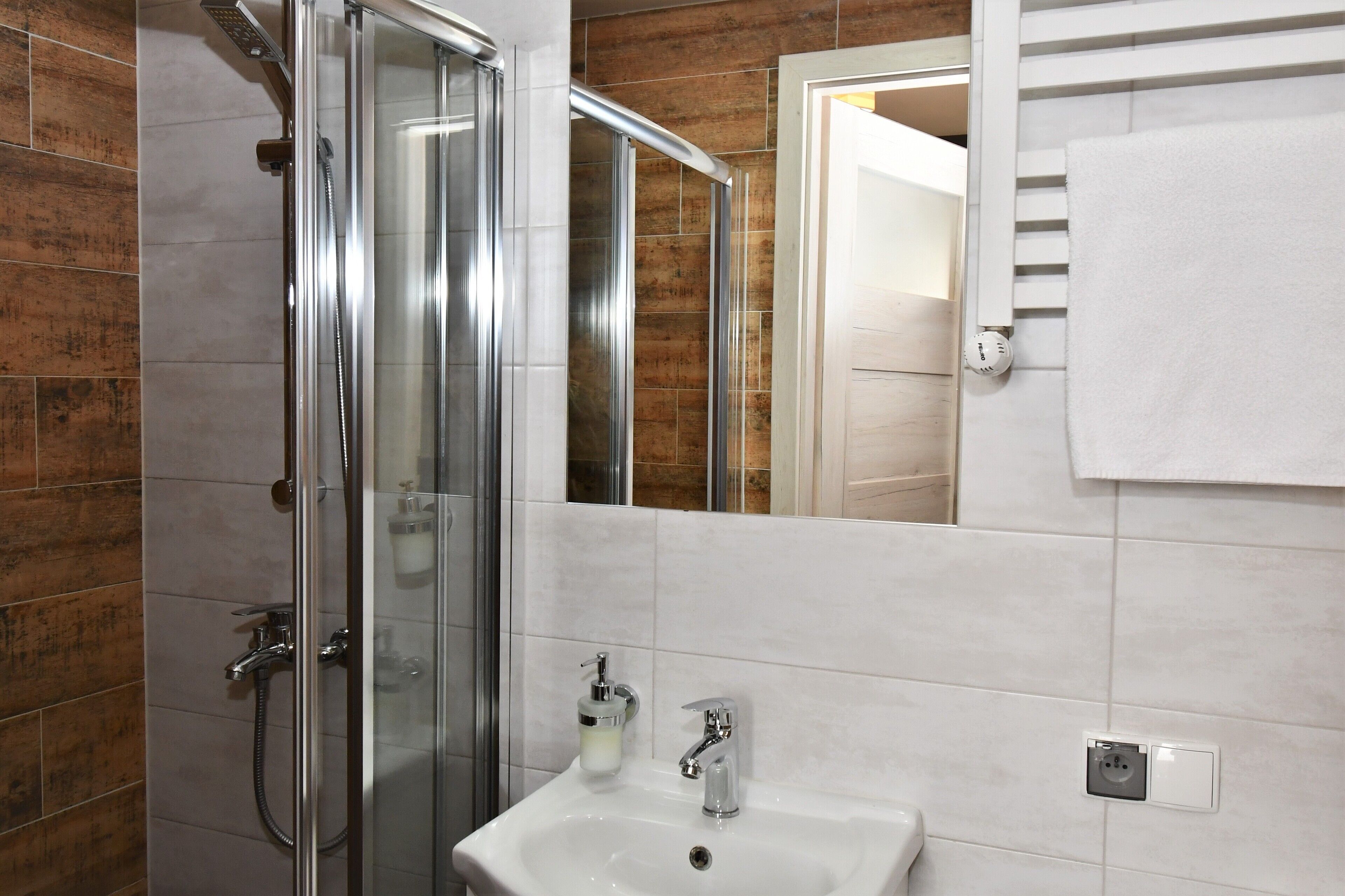 A bathroom with a glass shower enclosure, a white sink with a soap dispenser, and a towel hanging on a rack.