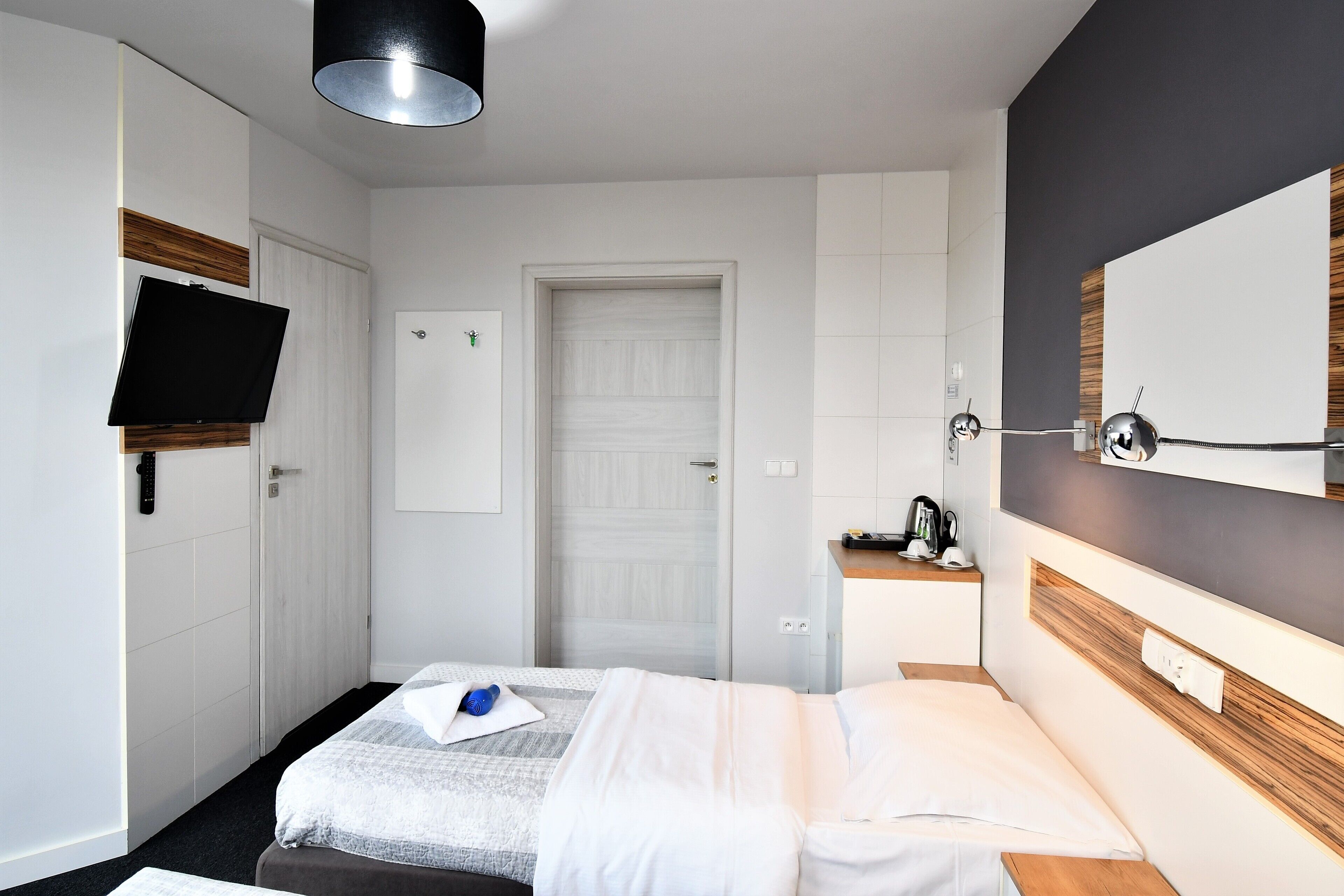 A hotel room with a bed, a TV mounted on the wall, a door, and a small table with a kettle.