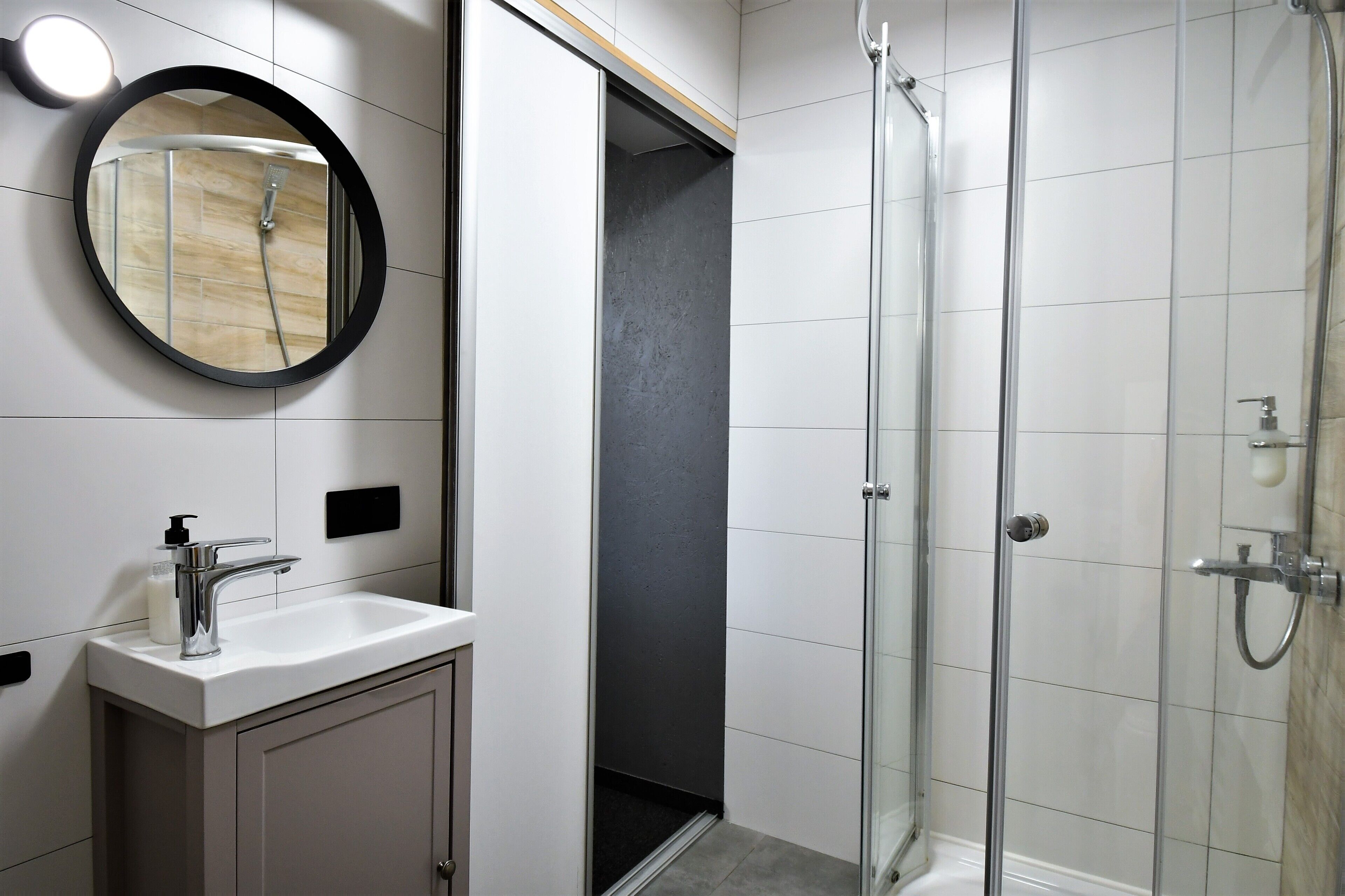 Un baño moderno con un espejo redondo, un lavamanos y una ducha con mampara de vidrio.