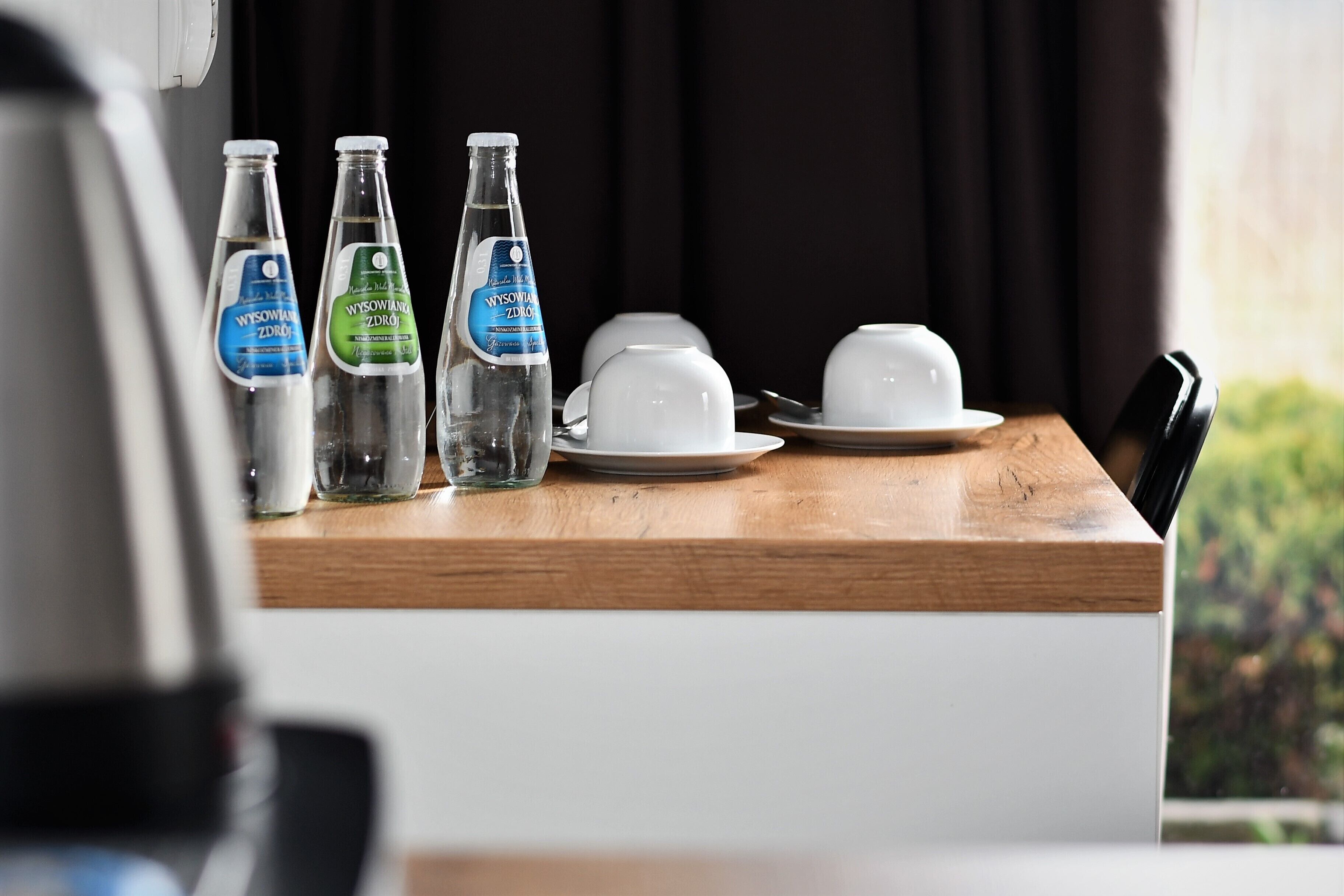 A wooden table with three bottles of water, a white cup, and a saucer.