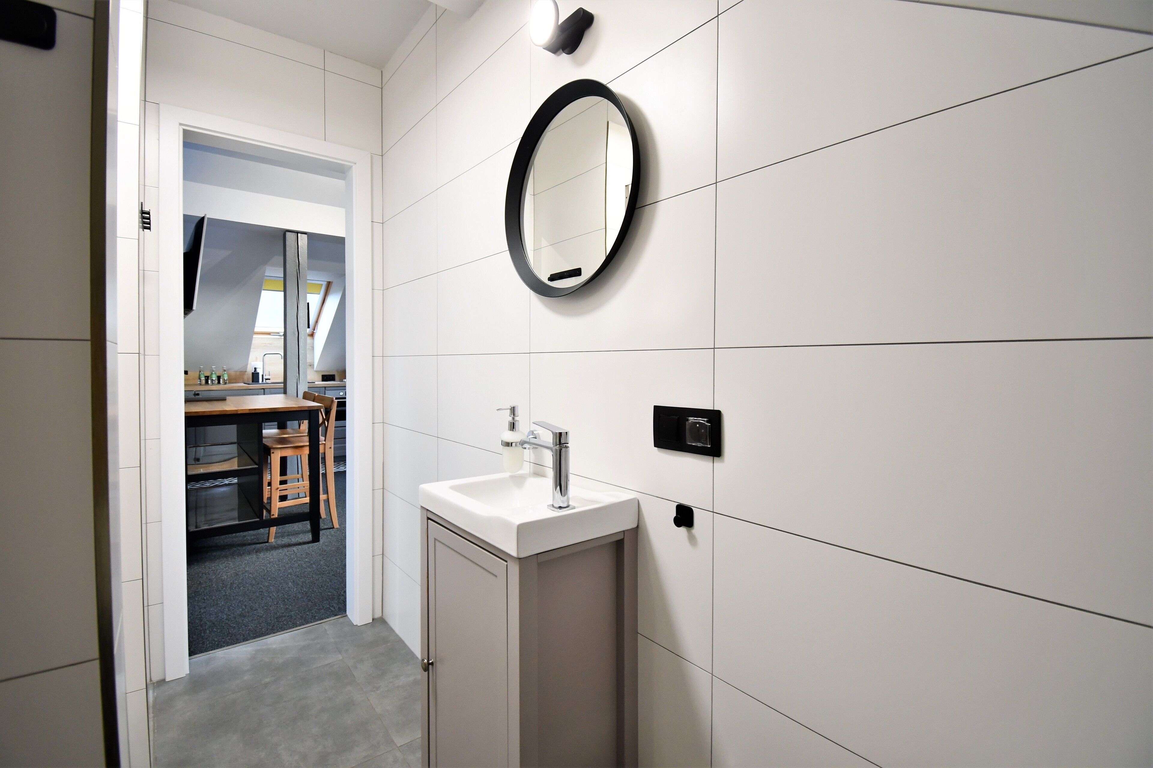 A modern bathroom with a white sink, a mirror, and a small window.