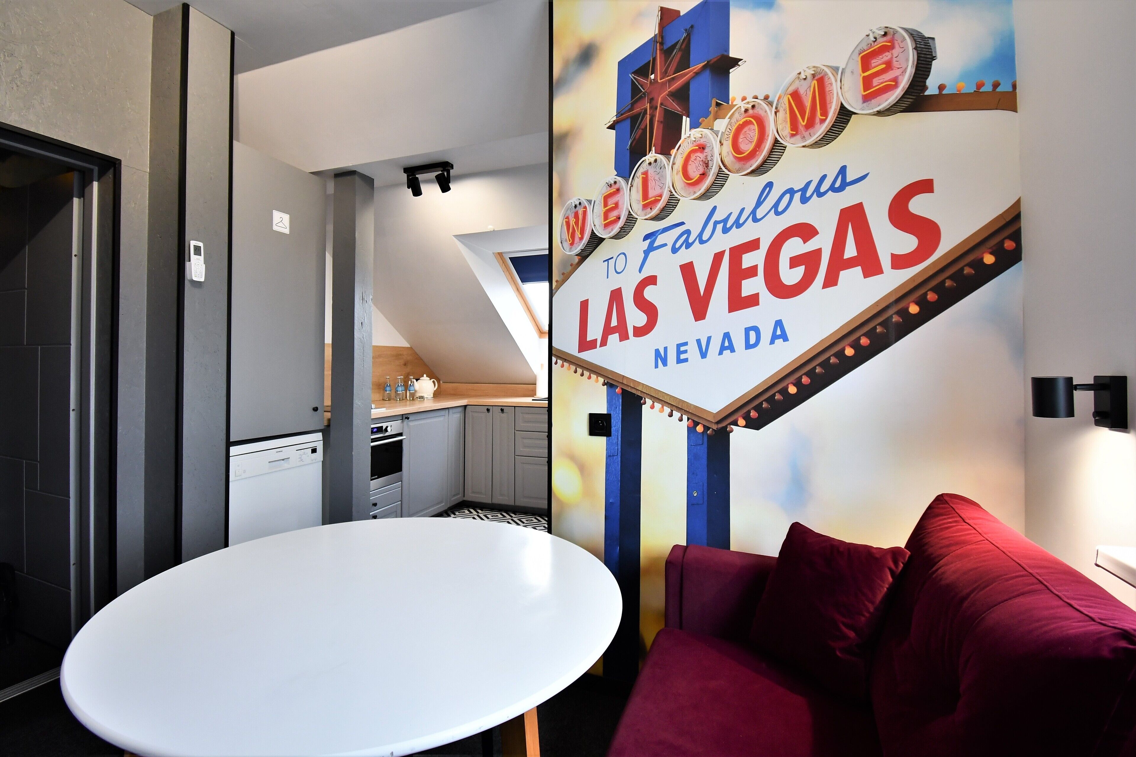A hotel room with a 'Welcome to Fabulous Las Vegas Nevada' sign, a white round table, and a red sofa.