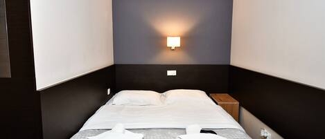 Una cama bien hecha con sábanas blancas, una manta a cuadros gris y blanco y dos toallas dobladas sobre la cama.