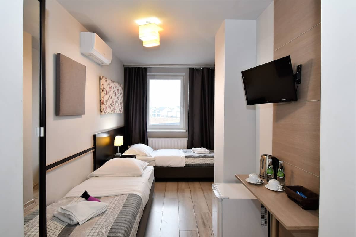 Una habitación de hotel con dos camas, un televisor, un escritorio pequeño con cafetera y una ventana con cortinas.
