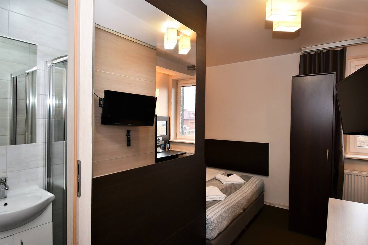 Habitación de hotel compacta con cama, mesita de noche, espejo, televisión y ventana.