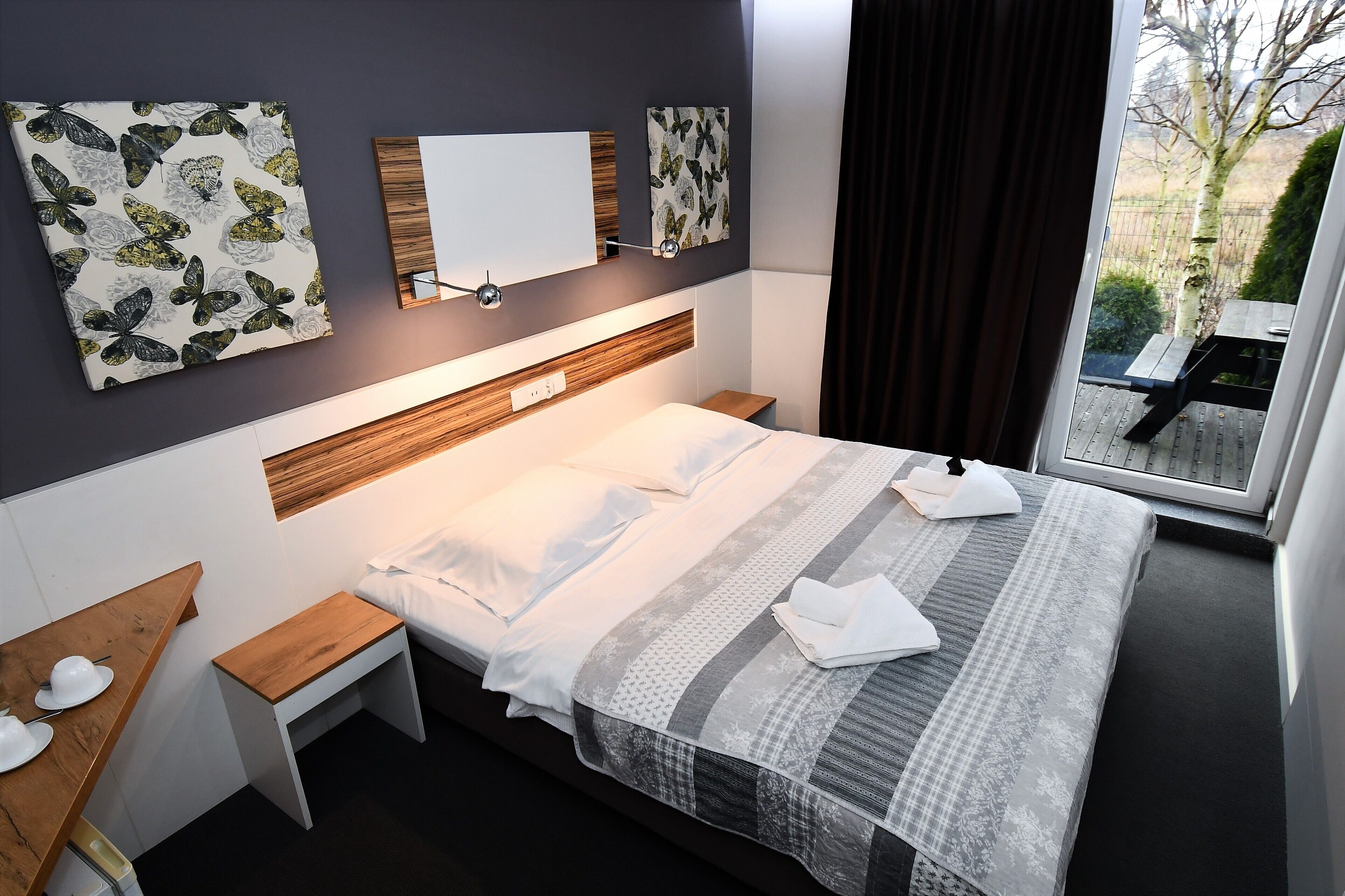 A modern hotel room with a large bed, bedside tables, a wooden bench, and a view of the outdoors.
