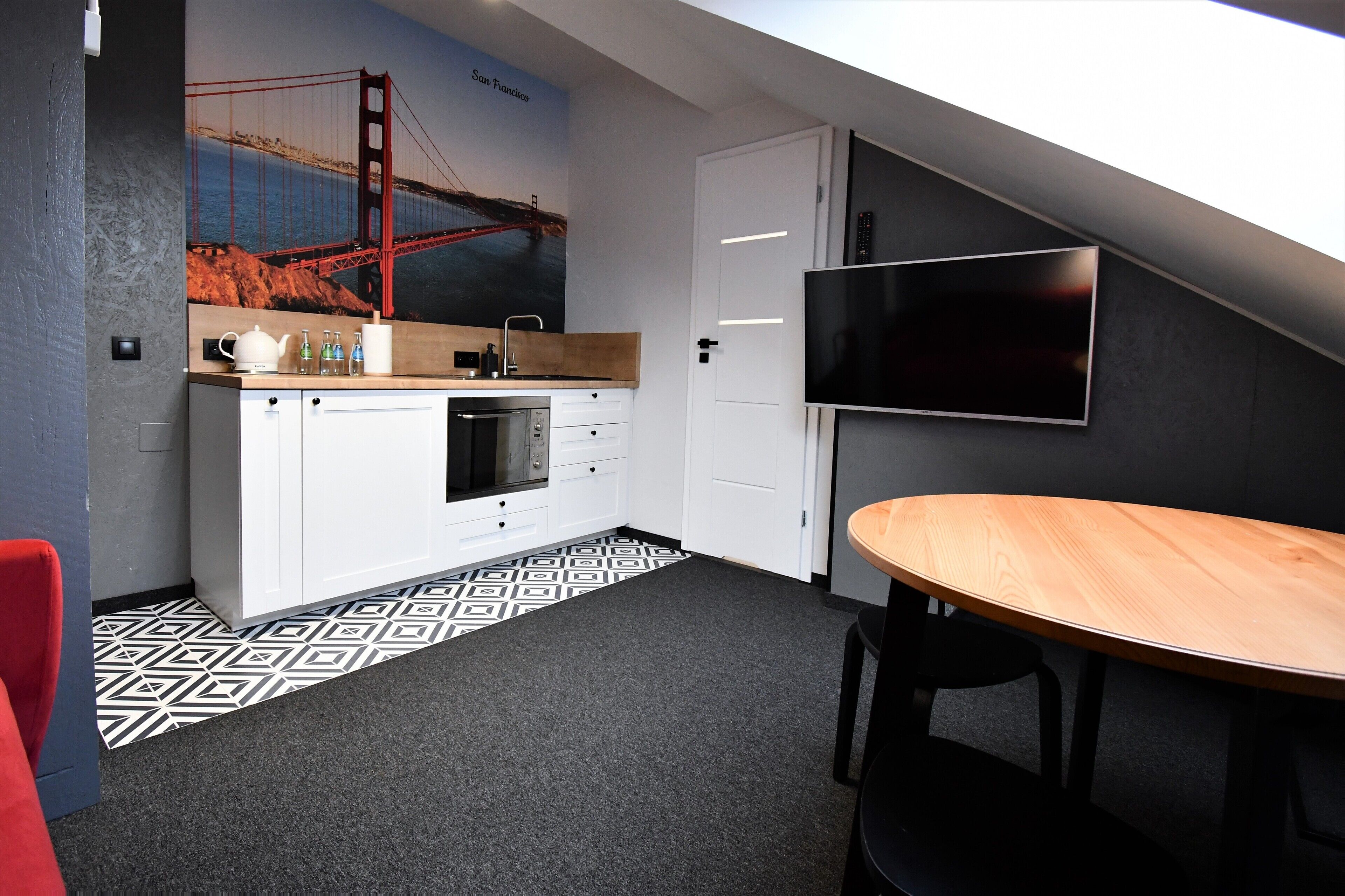 A modern kitchen with a large window, a flat-screen TV, and a dining area with a round table.
