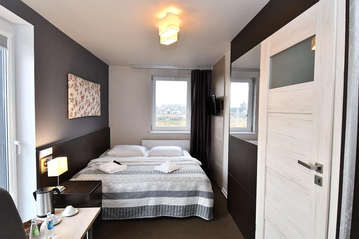 Habitación de hotel con cama, mesita de noche, lámpara y vistas al exterior.