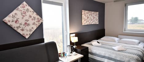 Una habitación de hotel con cama, mesita de noche, lámpara y un amplio ventanal.