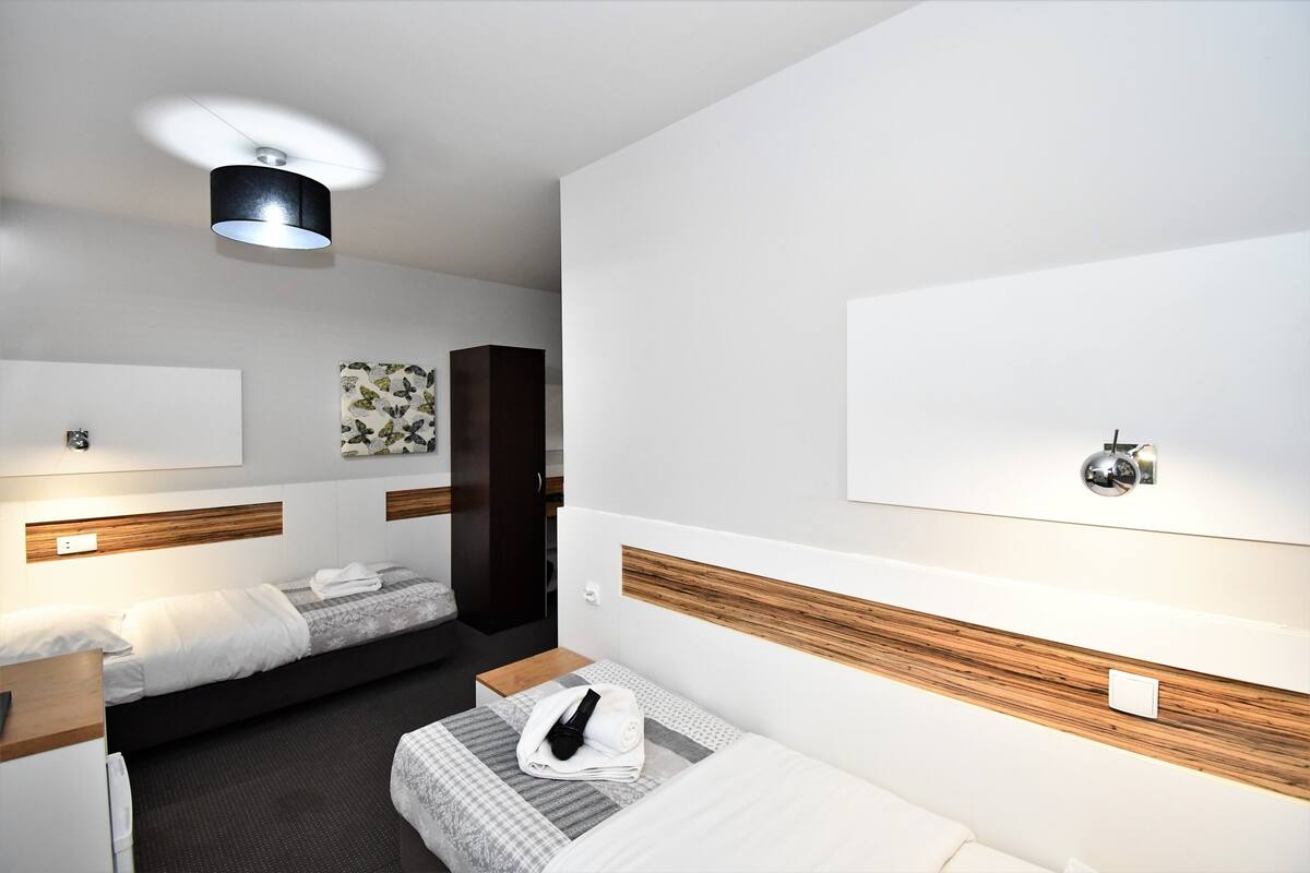 Una habitación de hotel moderna con dos camas, un cabecero de madera, un televisor montado en la pared y una lámpara del techo.
