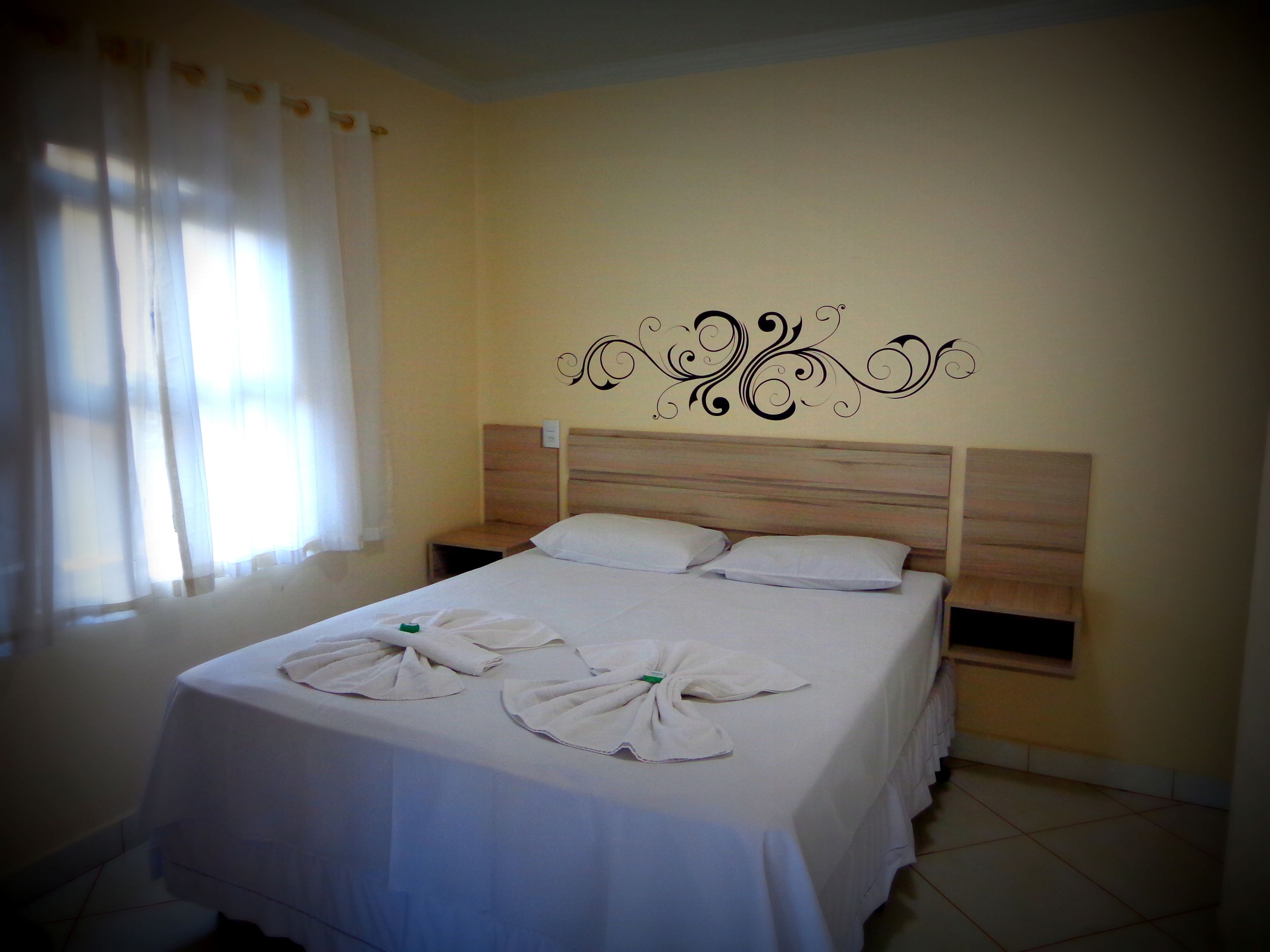 Cama bem arrumada com toalhas, cabeceira de madeira e um objeto decorativo na parede.