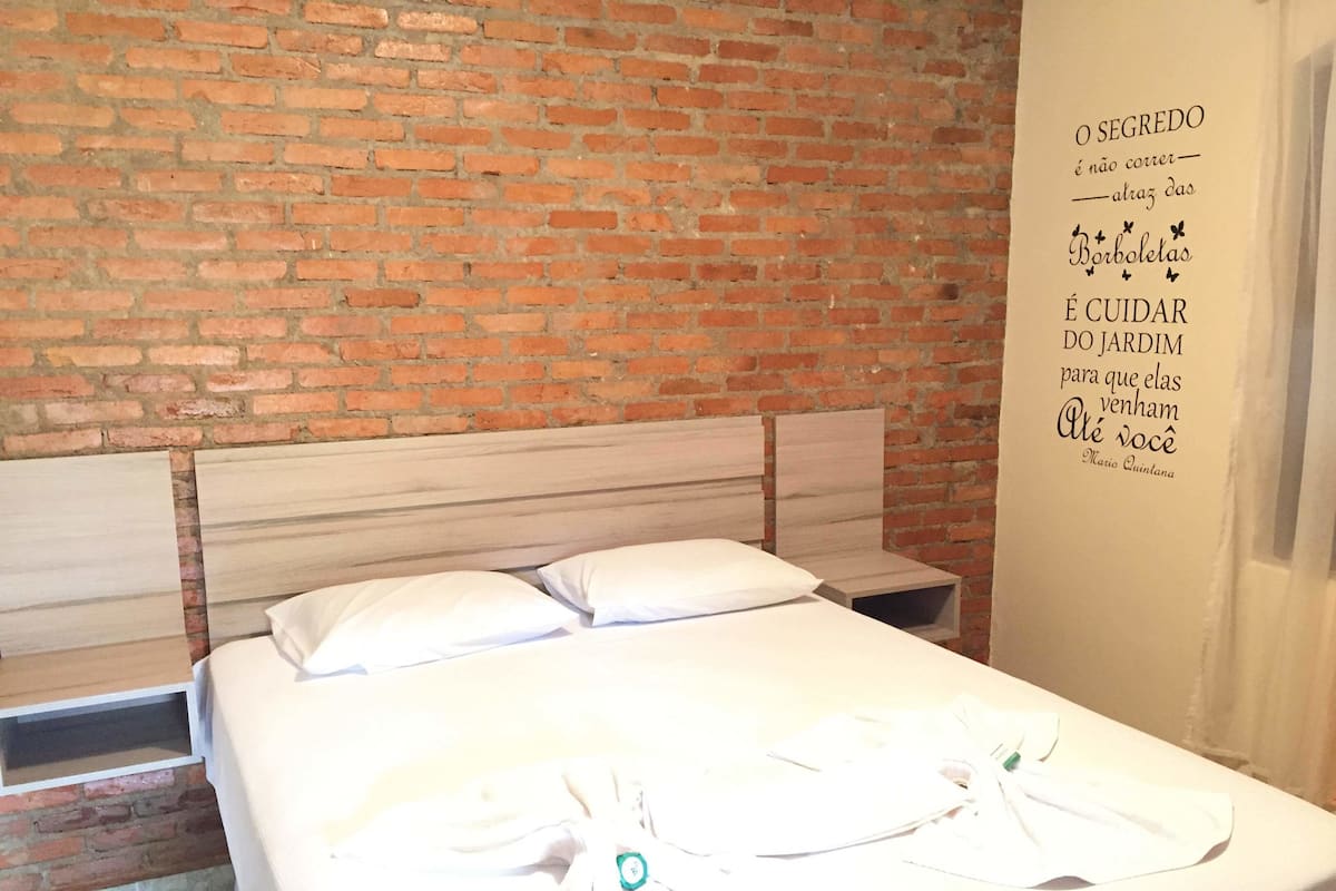 Une chambre d’hôtel avec un mur en briques, un lit en bois avec une literie blanche et une citation affichée sur le mur.