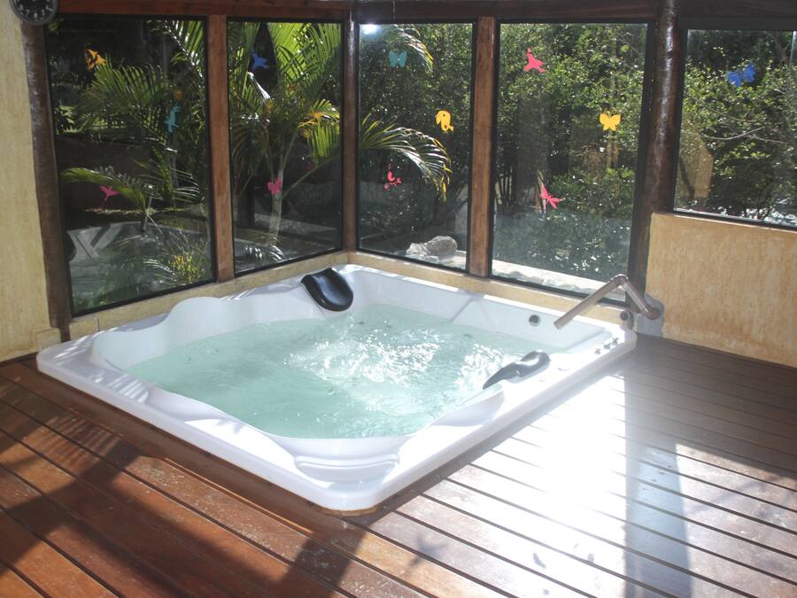 A hot tub in a room with large windows overlooking a garden.