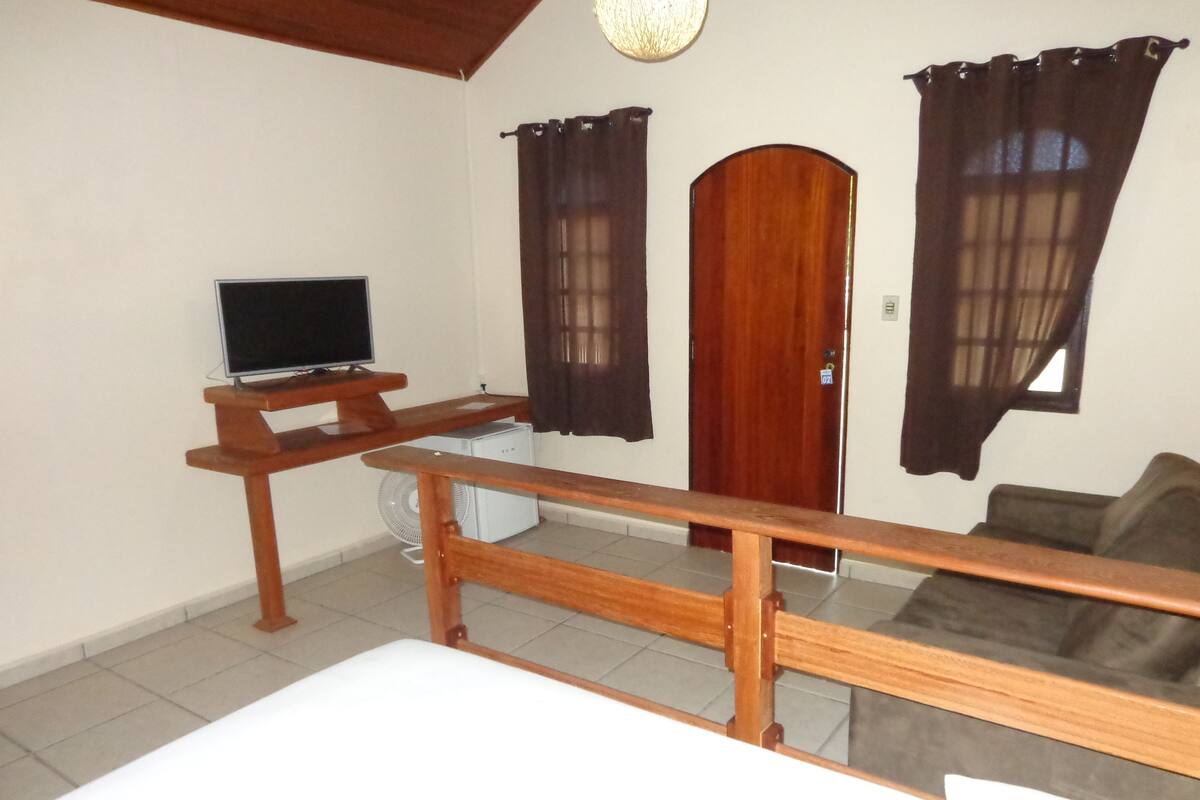 Une pièce avec un bureau en bois, une télévision, un canapé blanc et une porte avec des rideaux.