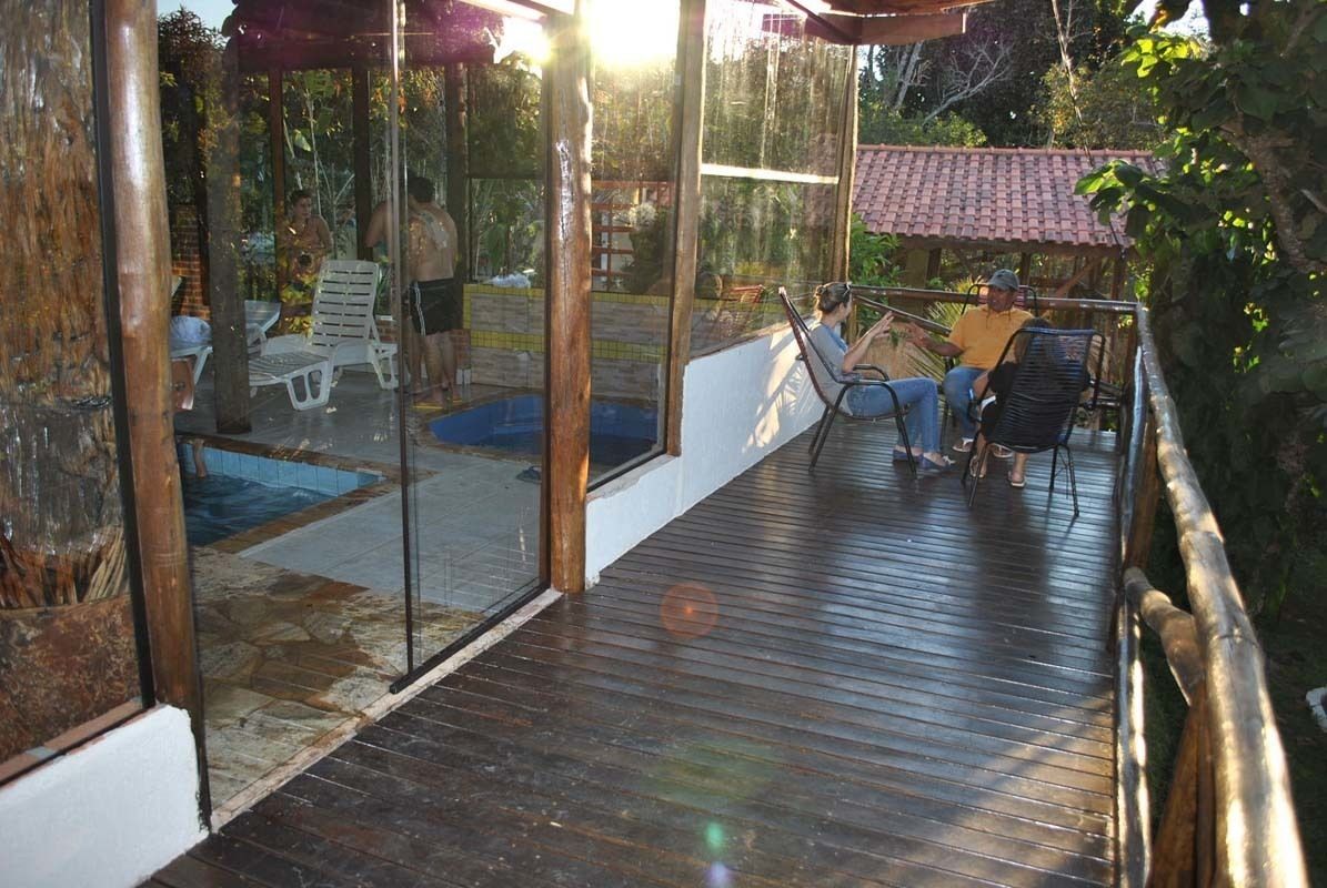 Um deck de madeira com estrutura de vidro, uma piscina e área de estar externa.