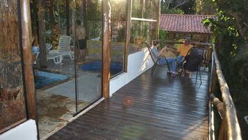 Um deck de madeira com estrutura de vidro, uma piscina e área de estar externa.