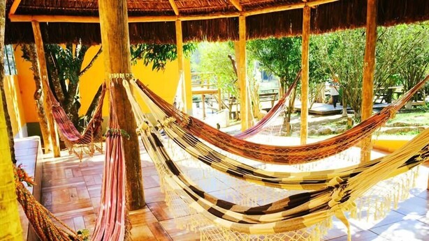 A hammock suspended between wooden pillars in a covered outdoor area with tiled flooring and a view of greenery outside. - Pousada Bezerra (Nazare Paulista)