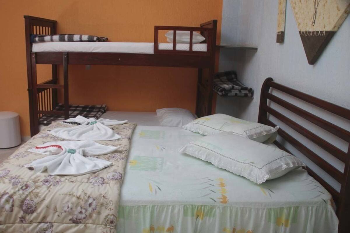Une chambre avec un lit superposé, une couvre-lit à motifs floraux, des oreillers et une petite étagère avec des livres.