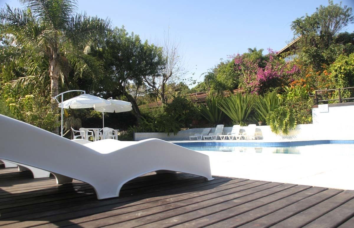 A wooden deck with a white lounge chair and a small pool area with lounge chairs and umbrellas.
