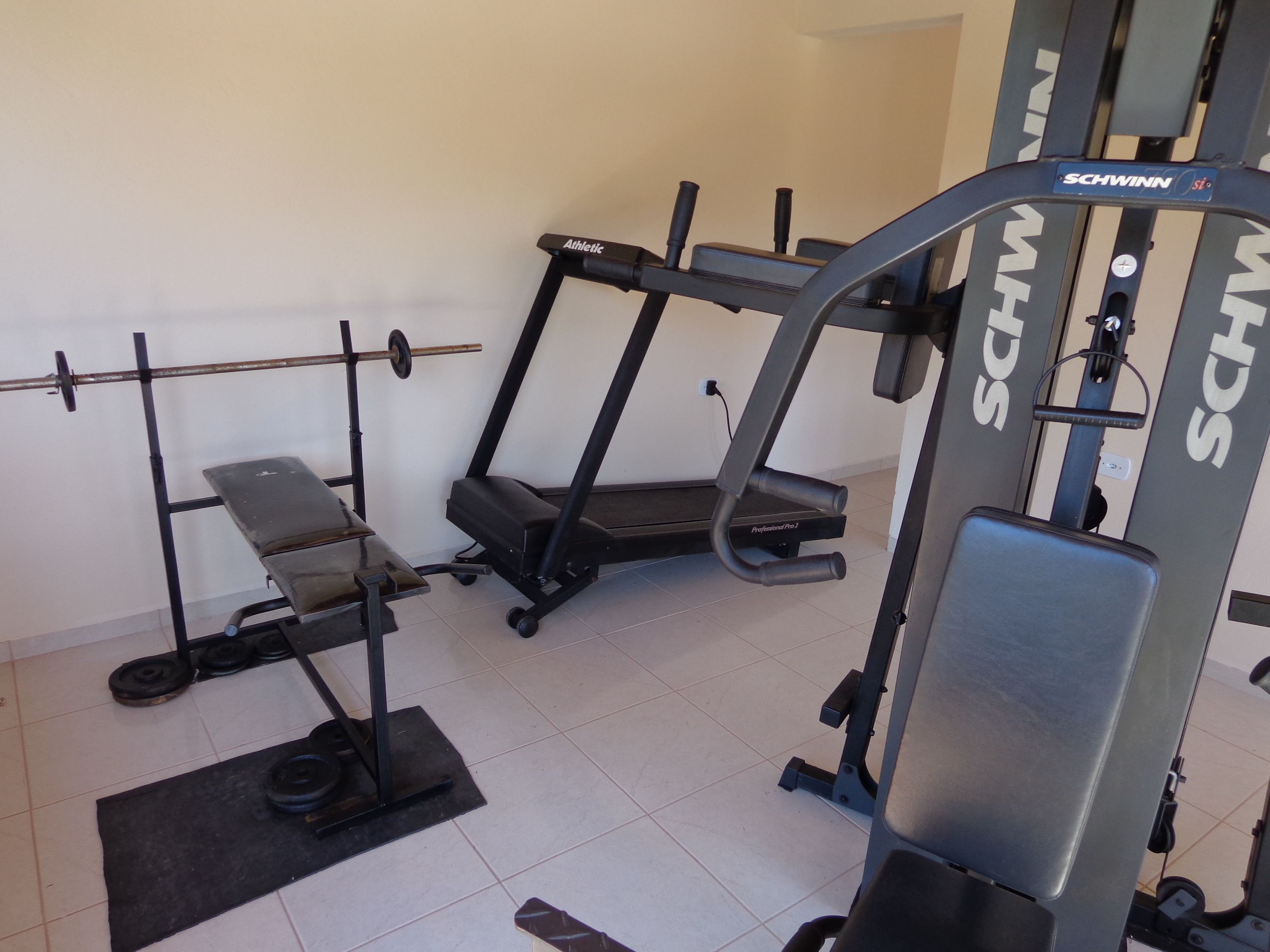 A gym with a treadmill, weight bench, and barbell rack.