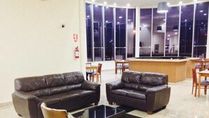 A lobby with two leather sofas, a glass coffee table, and a reception desk. - Habitat Hotel Pirassununga (Pirassununga)
