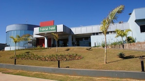 A modern hotel with a prominent 'habitat hotel' sign, a curved glass building, and landscaped grounds with palm trees. - Habitat Hotel Pirassununga (Pirassununga)