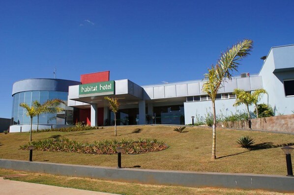 A modern hotel with a prominent 'habitat hotel' sign, a curved glass building, and landscaped grounds with palm trees. - Habitat Hotel Pirassununga (Pirassununga)