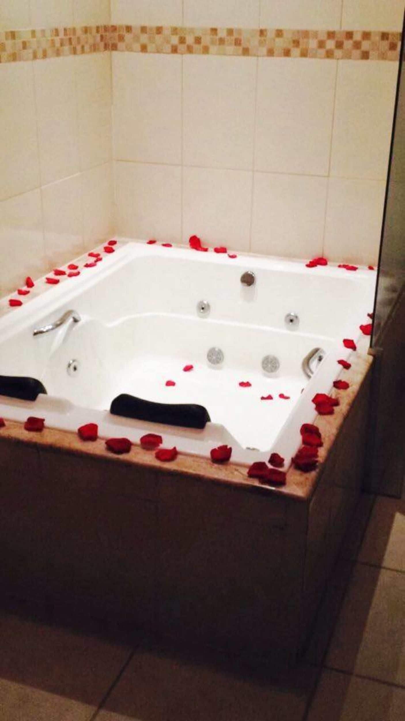 A square bathtub filled with rose petals, with a tiled wall and a glass shower door in the background.