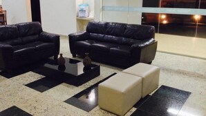 A modern lobby with two black leather sofas, a glass partition, and a view of the sunset through the window. - Habitat Hotel Pirassununga (Pirassununga)