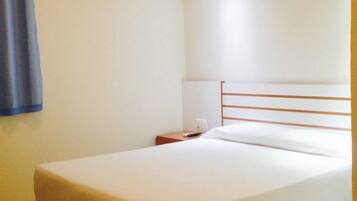 Habitación de hotel sencilla y limpia con una cama individual, una mesita de noche y una pared lisa.
