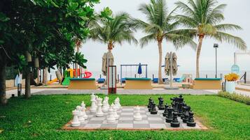 A chessboard set up outdoors with palm trees and beach chairs in the background.