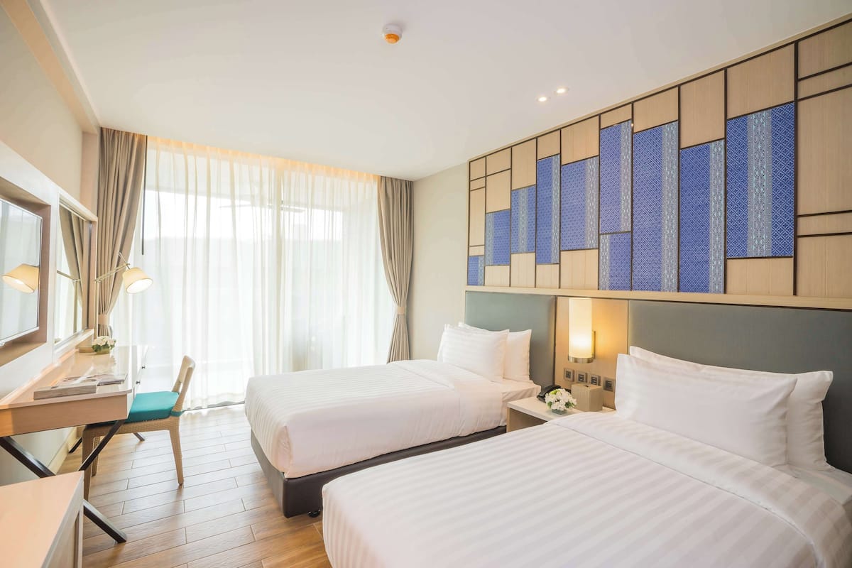 Een hotelkamer met twee bedden, een bureau, een stoel en een groot raam met gordijnen.
