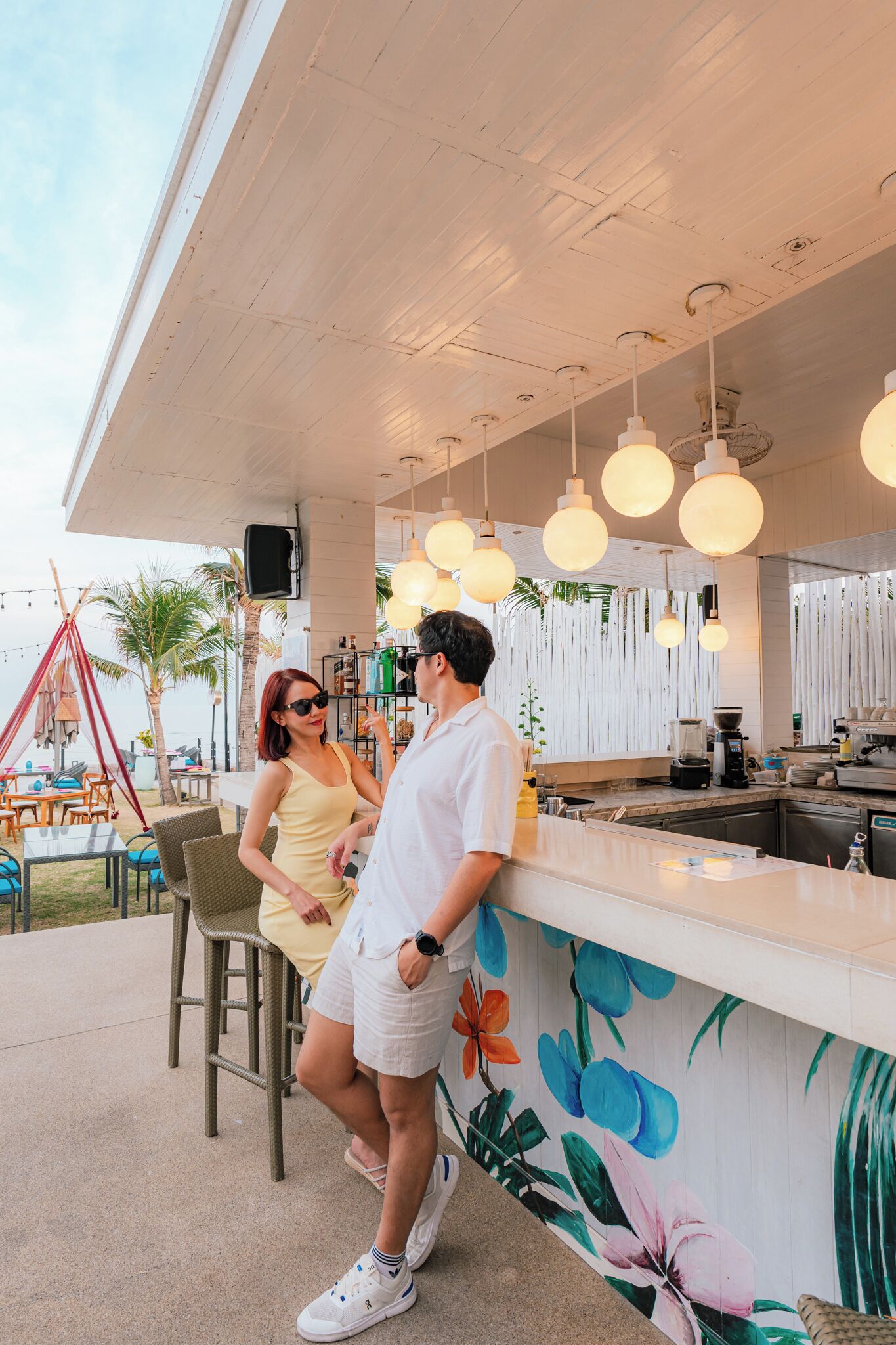 Un espace bar avec un comptoir, des luminaires suspendus et une fresque représentant des fleurs tropicales.