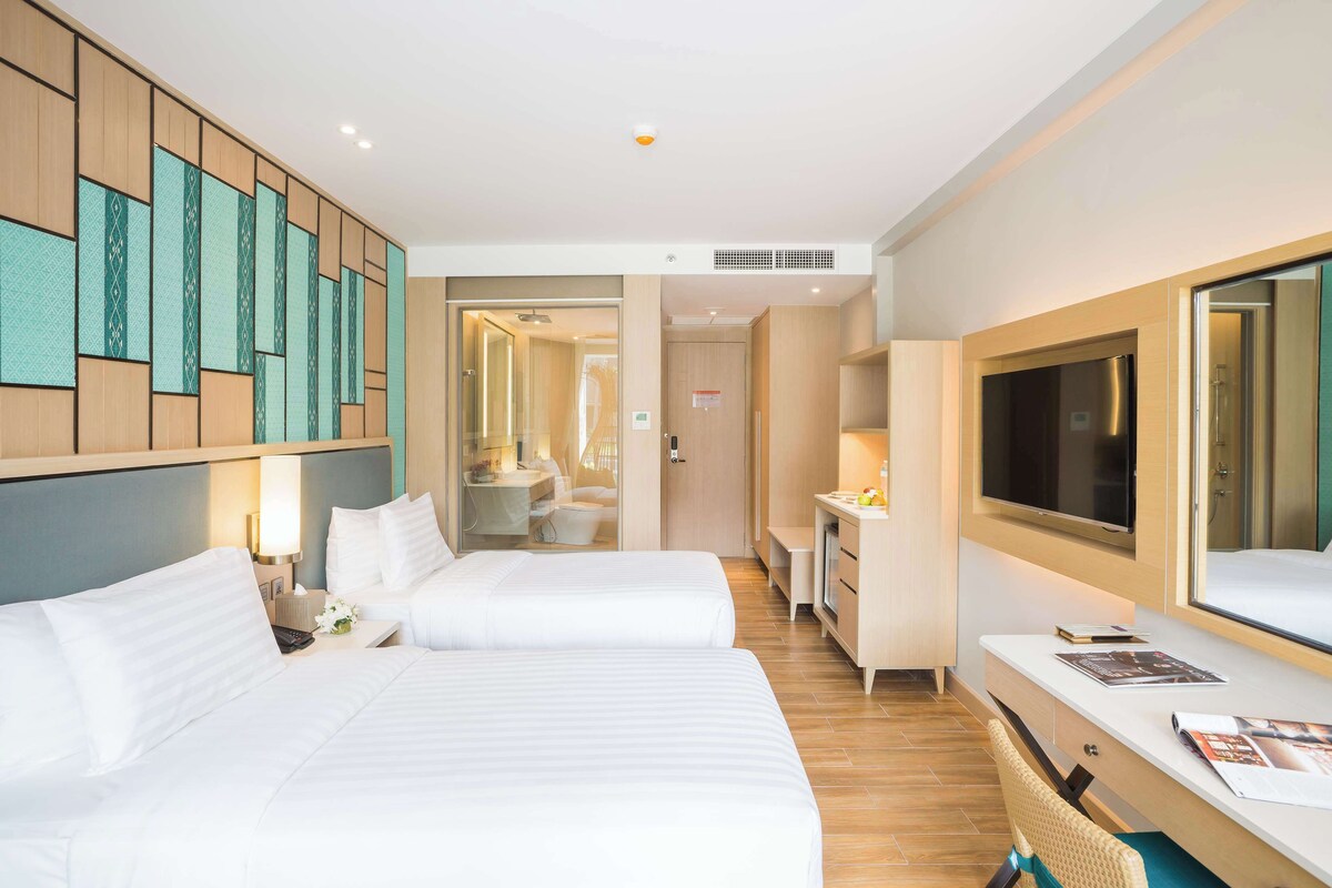 A hotel room with two beds, a desk, a TV, and a bathroom visible through an open door.