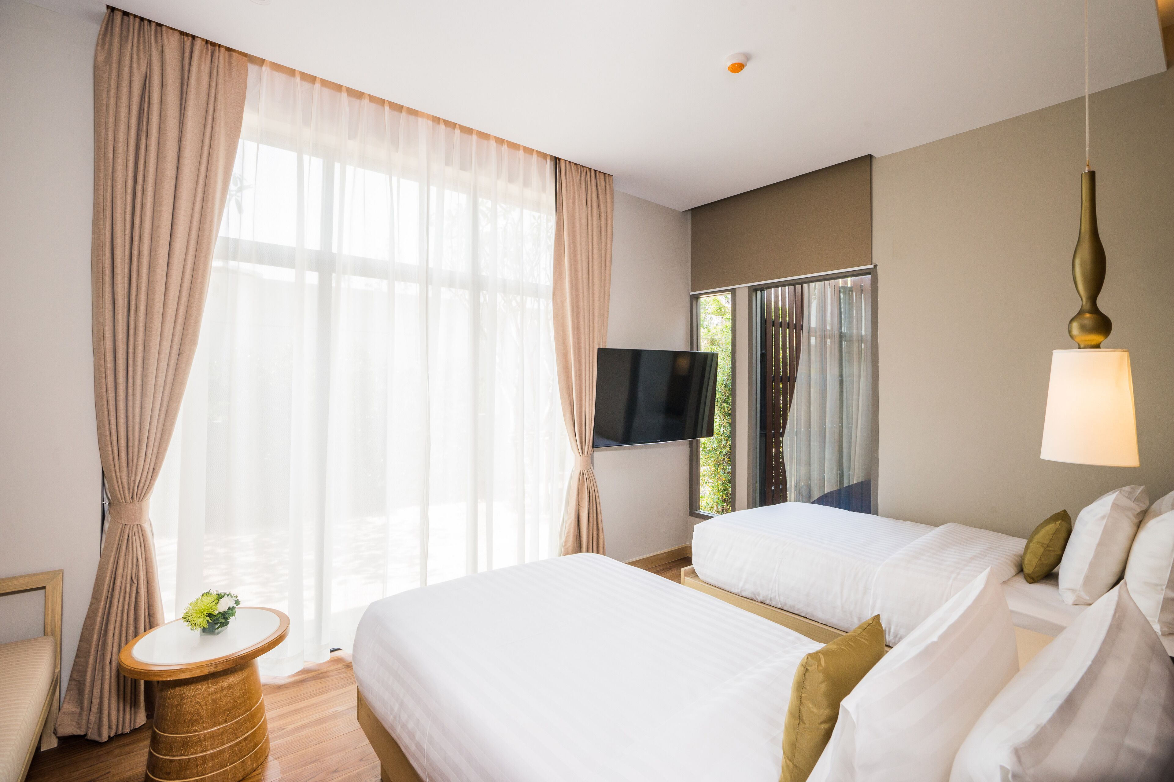 A hotel room with two beds, a TV, a window with curtains, a bedside table, and a lamp.