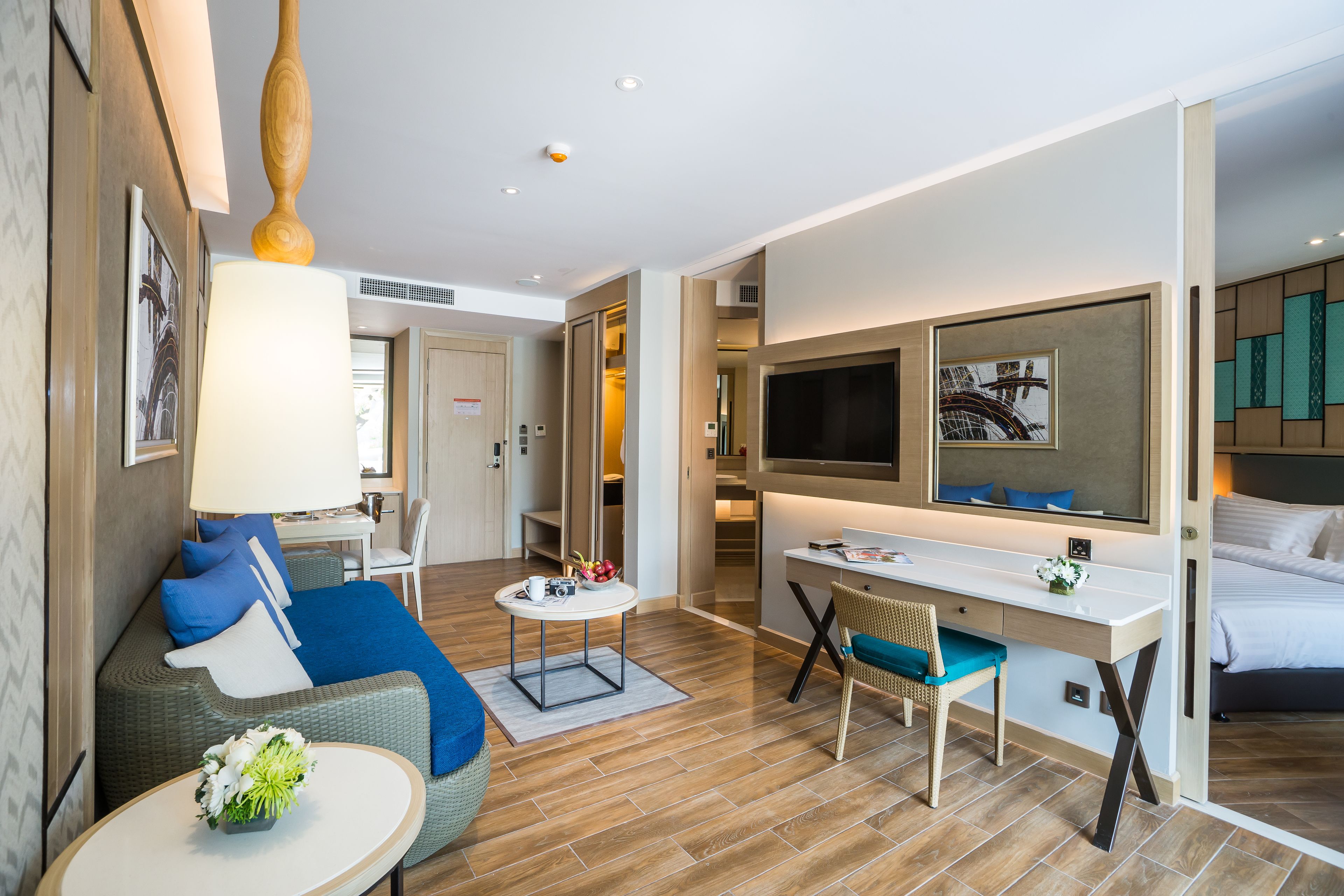 A modern hotel room with a sofa, a desk, a chair, a TV, and a bed.