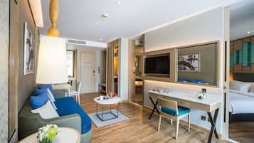 A modern hotel room with a sofa, a desk, a chair, a TV, and a bed.