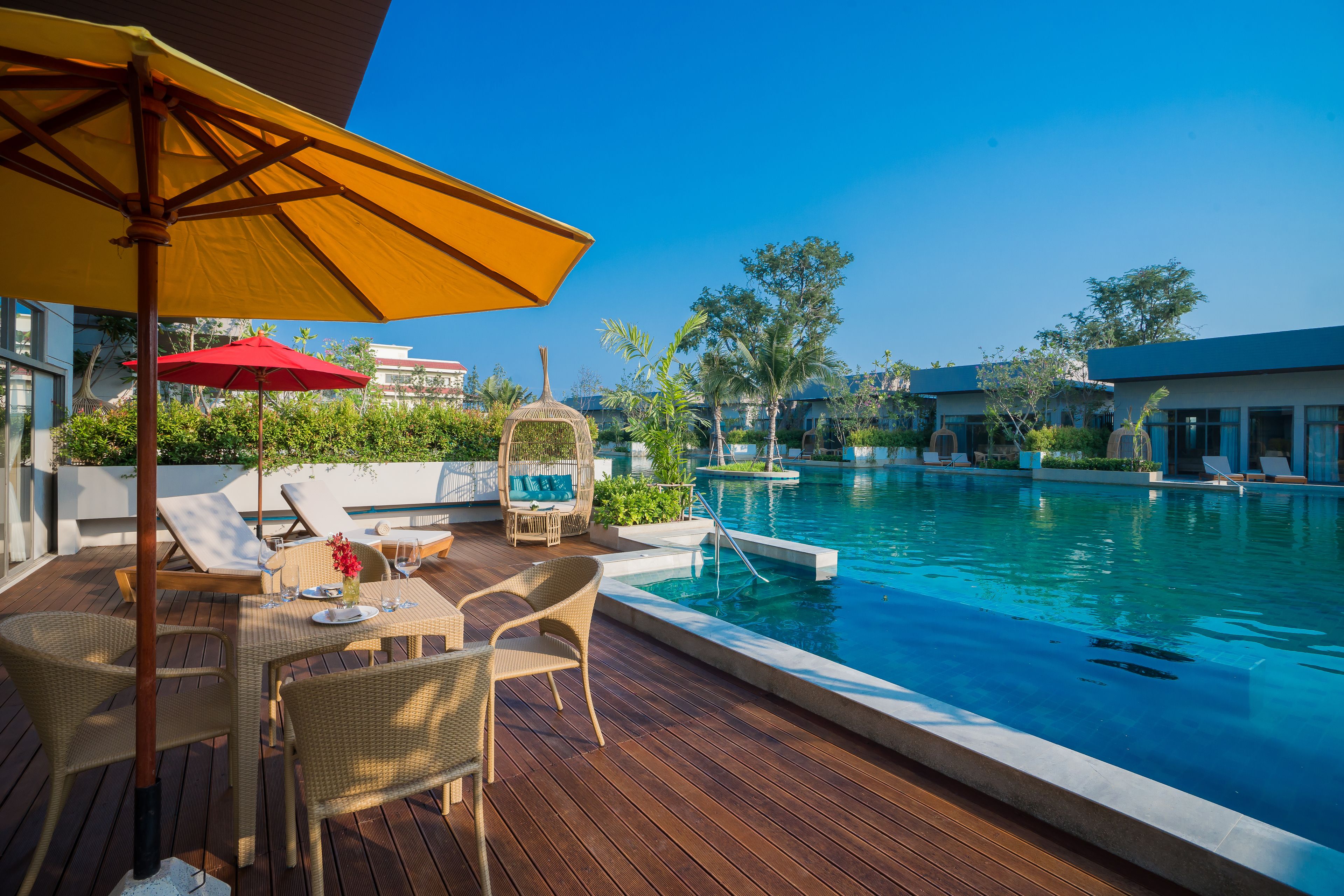 A poolside area with a wooden deck, lounge chairs, and a table with a red umbrella.