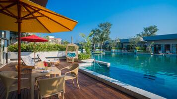 A poolside area with a wooden deck, lounge chairs, and a table with a red umbrella.