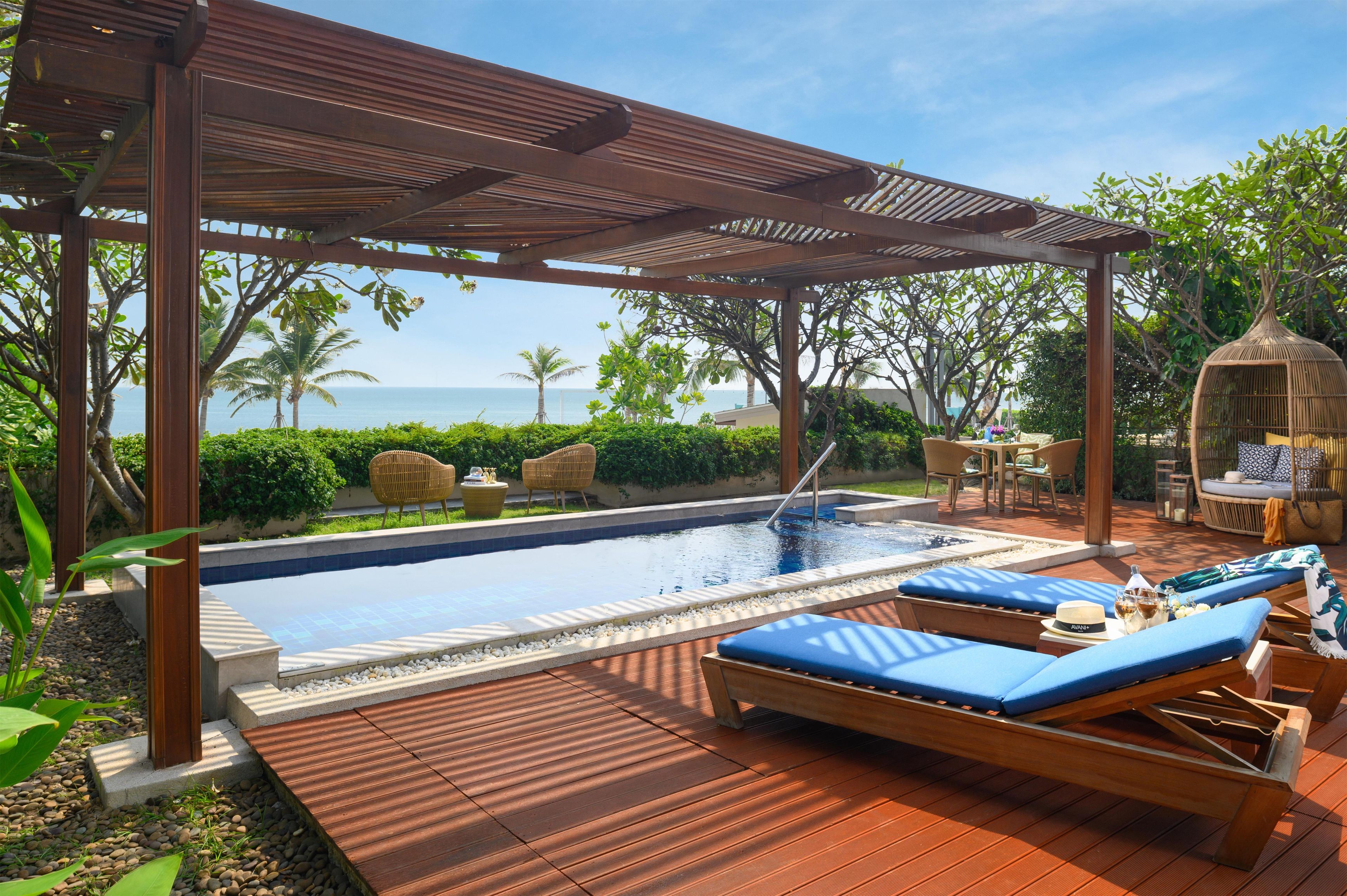 A pool area with a wooden deck, lounge chairs, and a view of the ocean.