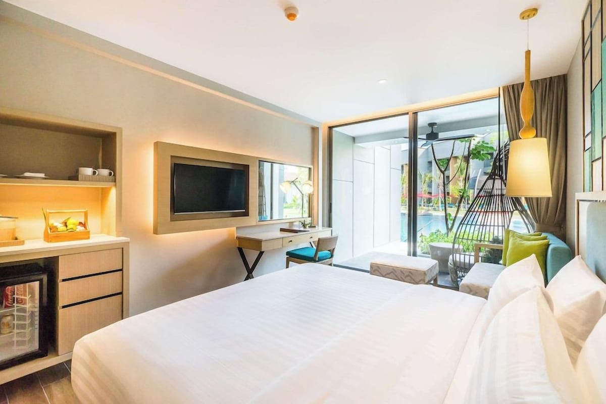 Habitación de hotel con cama, escritorio, televisión y balcón con plantas.