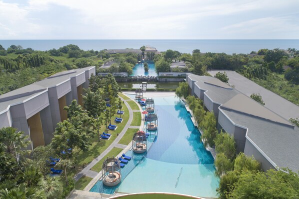 A resort with a long swimming pool, lounge areas, and a view of the sea.