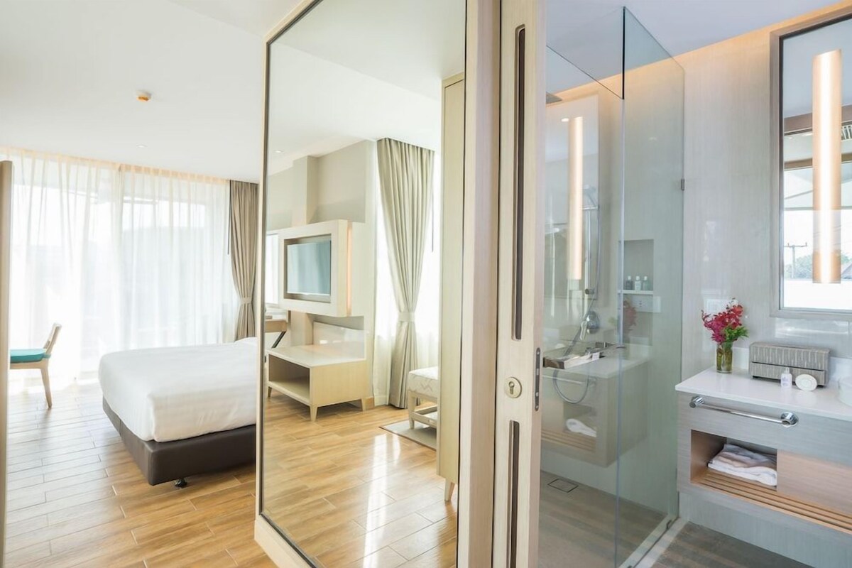 A modern hotel room with a bed, television, desk, and a glass-enclosed shower area.