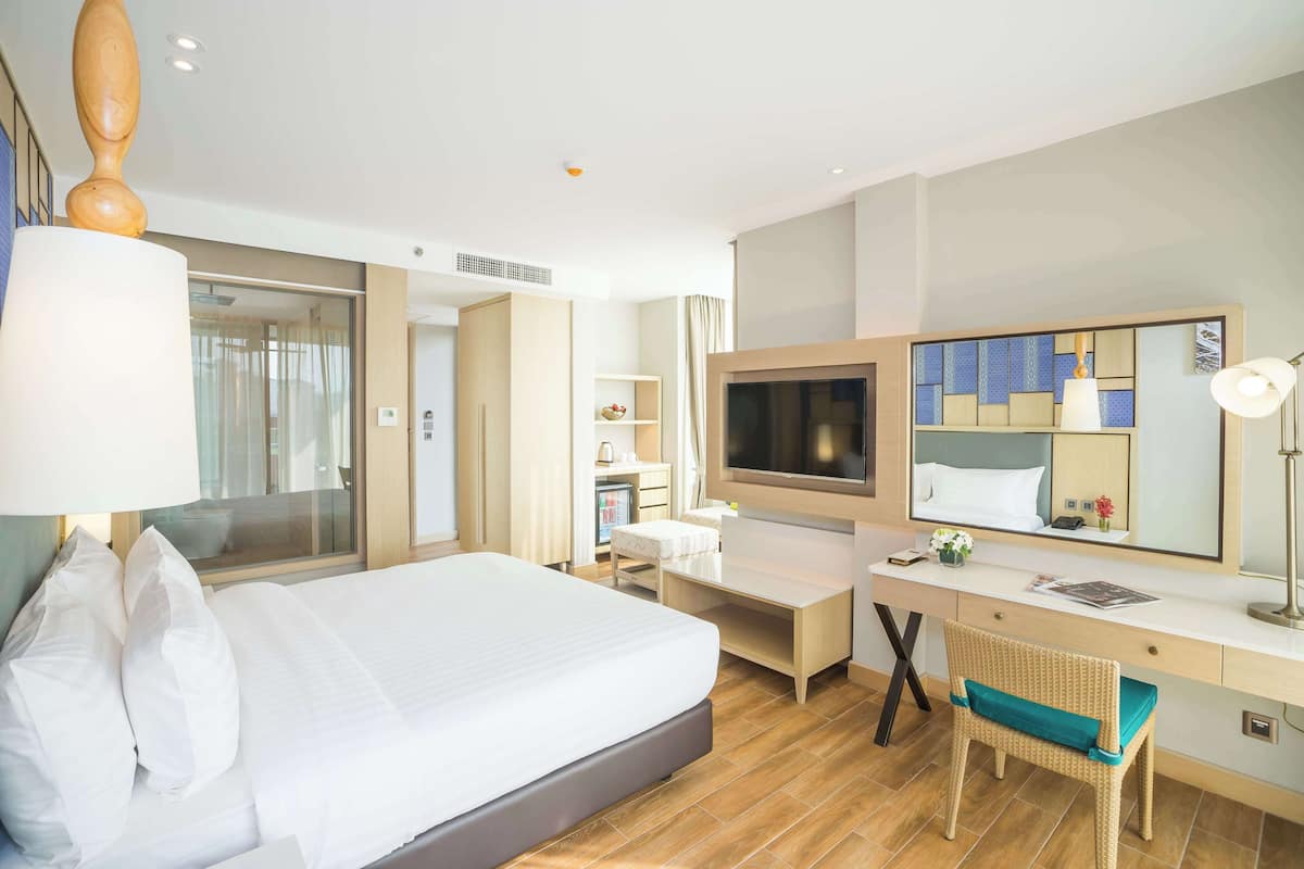 Een hotelkamer met een bed, een bureau, een stoel, een televisie en een grote spiegel.
