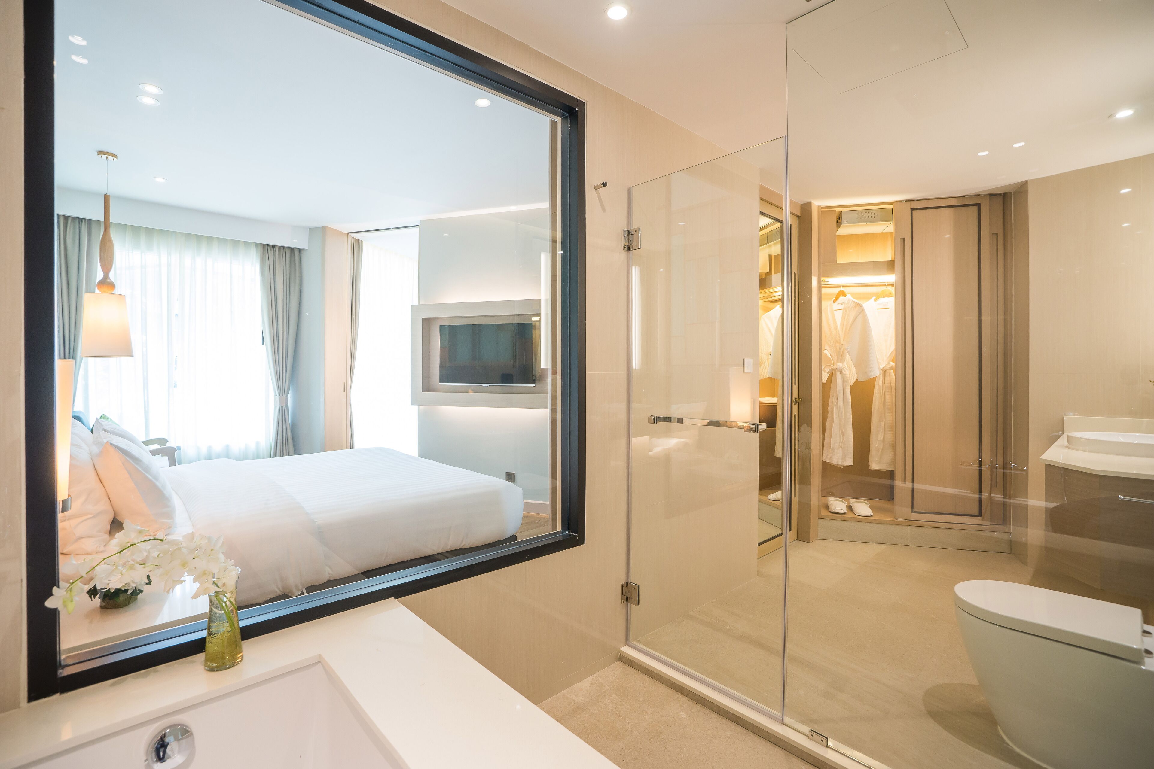 A modern hotel room with a large bed, a glass-enclosed shower, a white sink, and a mirror reflecting the room.