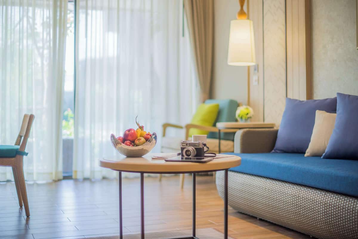 Een gezellige woonkamer met een blauwe bank, een ronde houten salontafel met een camera en een schaal fruit, een stoel en een lamp.