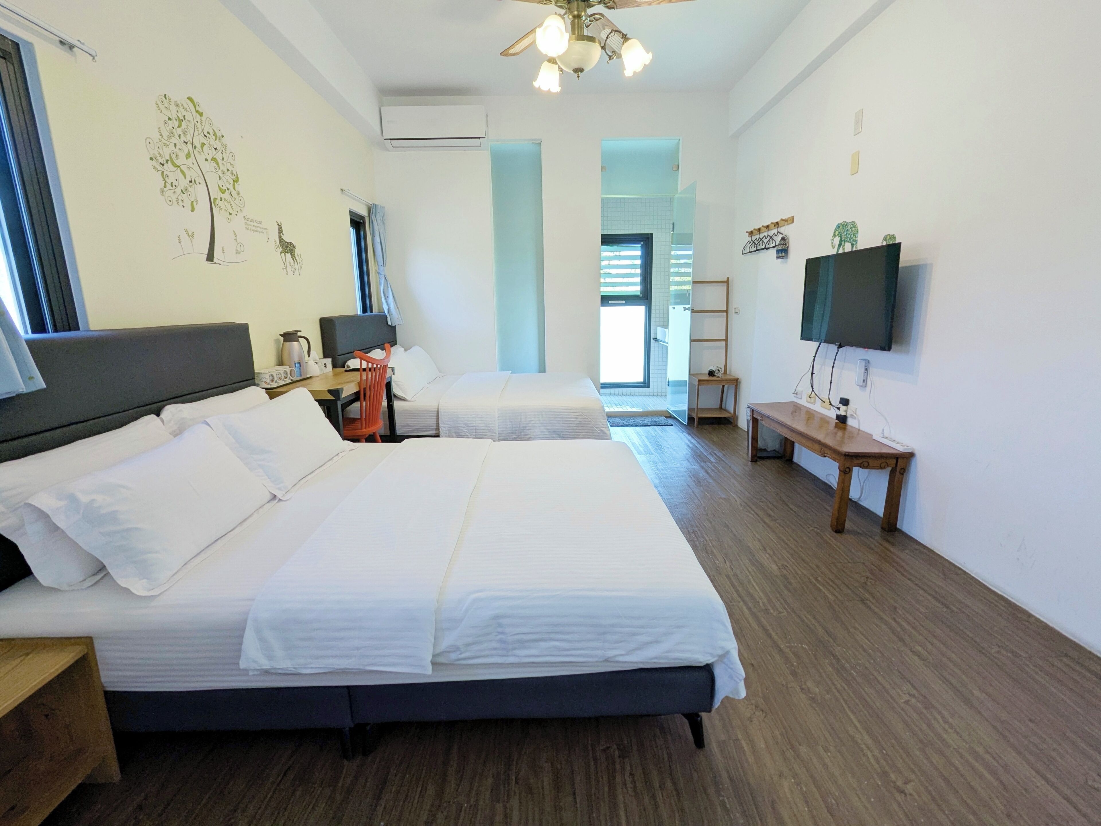 Une chambre d’hôtel avec deux lits, un bureau, une chaise, une télévision et une fenêtre.