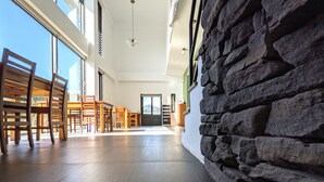Un pasillo amplio con sillas y mesas de madera, una pared de piedra y vistas al exterior.